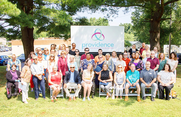 employees from providence sitting in front of a sign with a providence of maryland logo